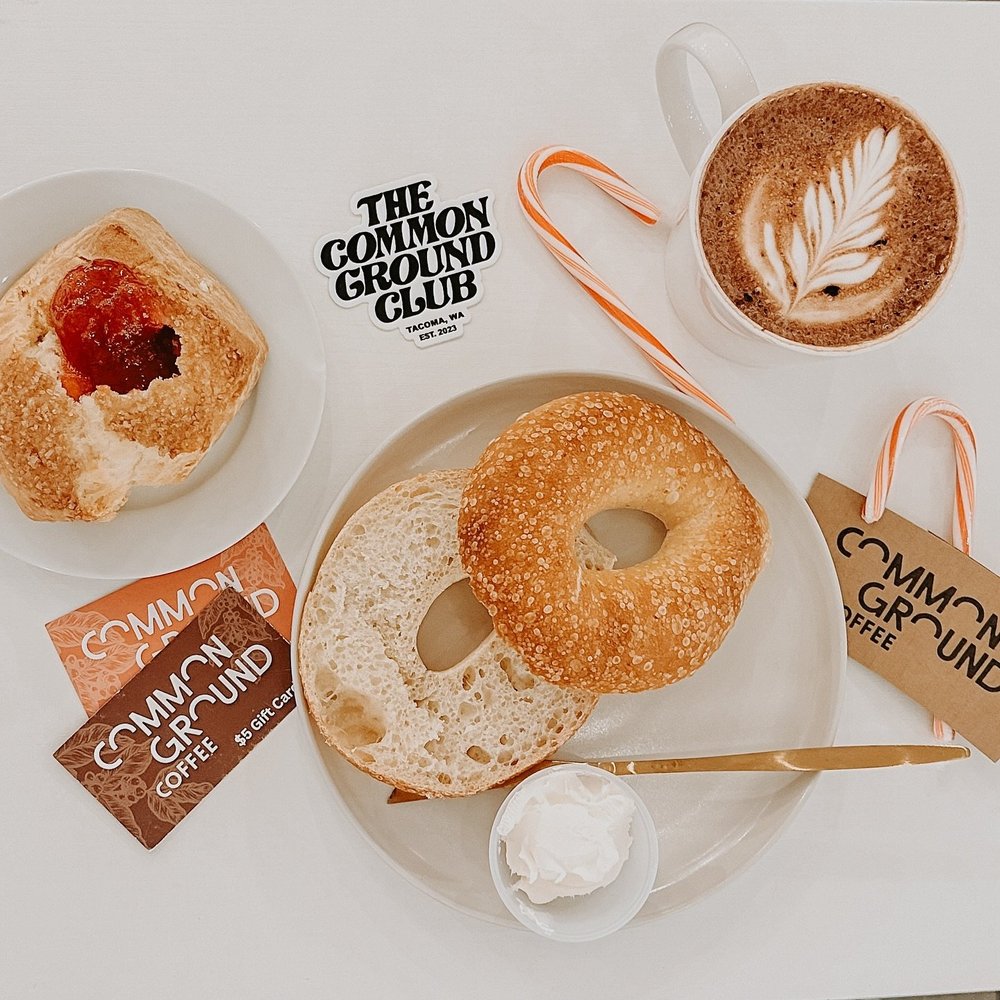 Latte art, bagel, and Common Ground Club Tacoma branded gifts flat lay